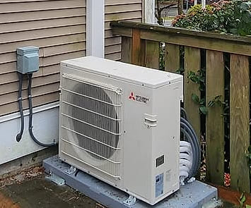 An outdoor unit standing on a pad beside its electrical disconnect.